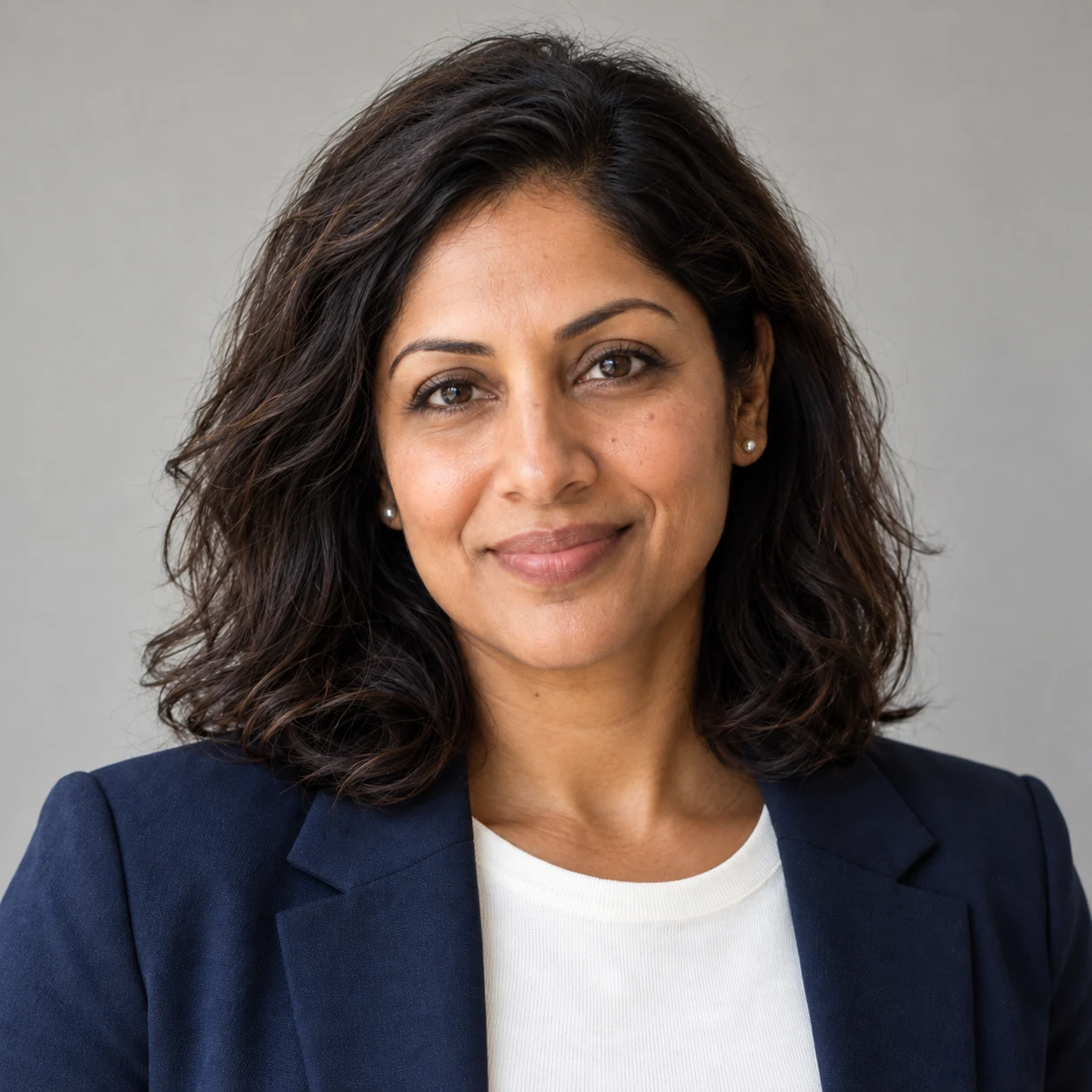 Aisha in a navy blazer with a neutral background — fictional AI example.